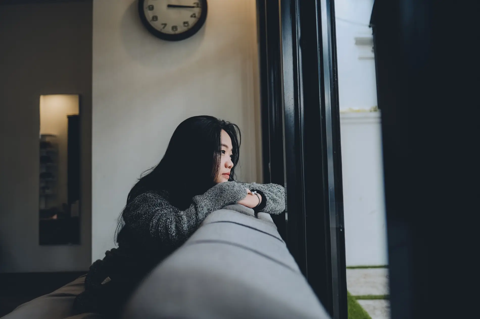 A woman resting her arms on a sofa, looking thoughtfully out of a window