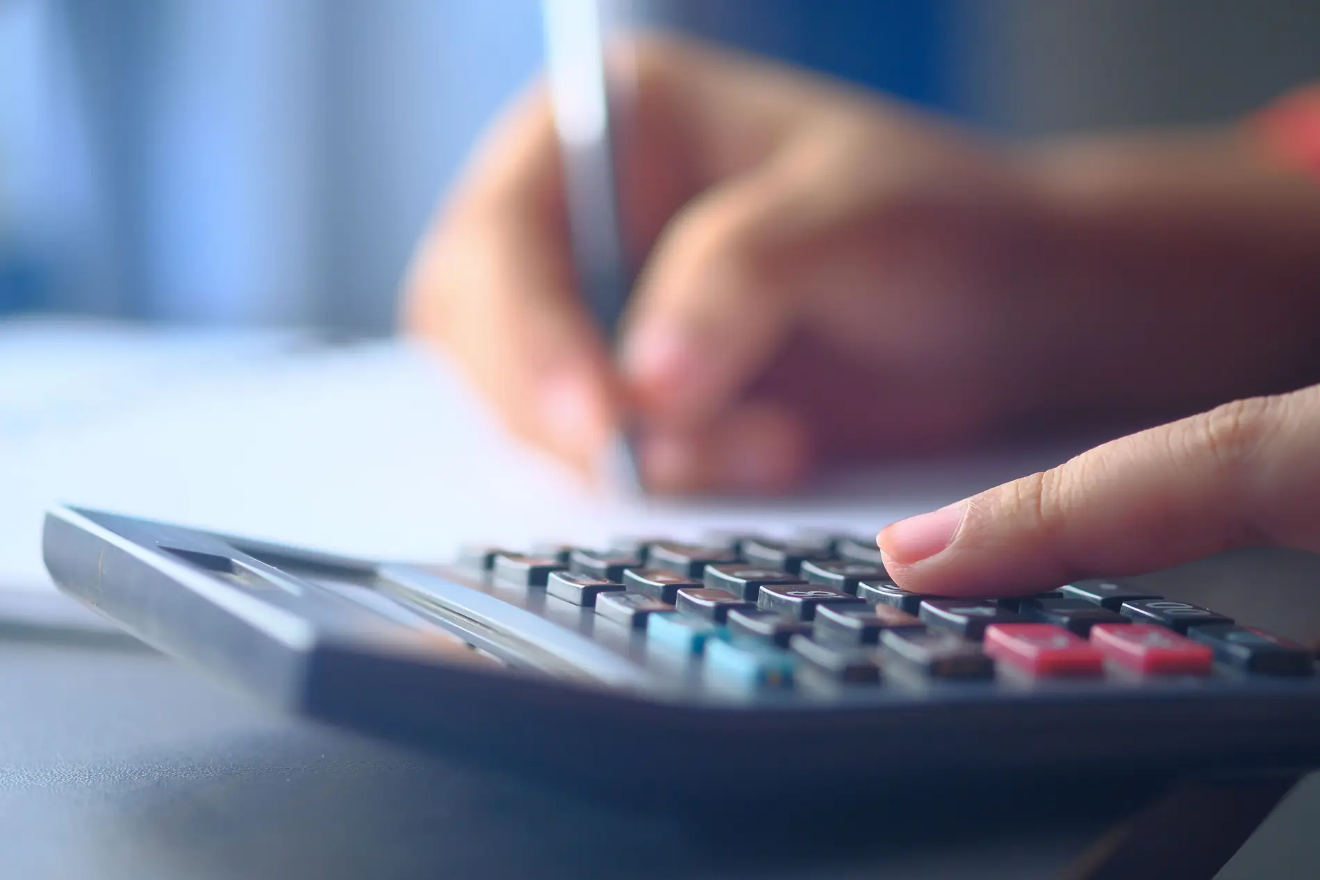 A close-up of a hand writing while calculating figures on a calculator